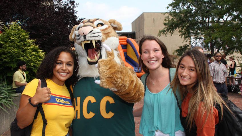 Three HCC students pose outside with the HCC Cougar mascot