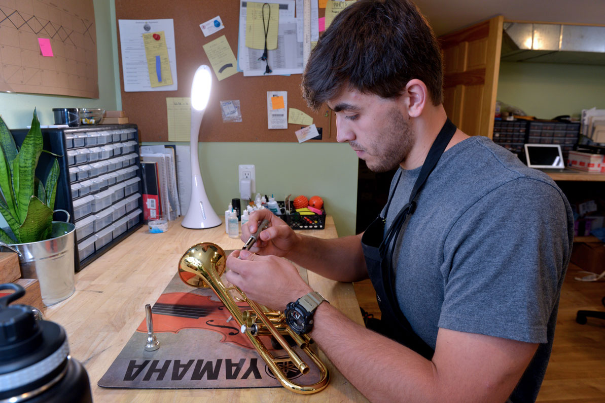 David works on a trumpet in the family's musical repair shop.