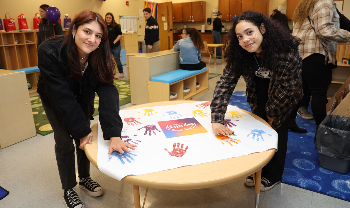 HCC students Alisson De La Fuente, left, and Gio Fernandez add their handprints to a montage during a holiday celebration for the Itsy Bitsy Child Watch
