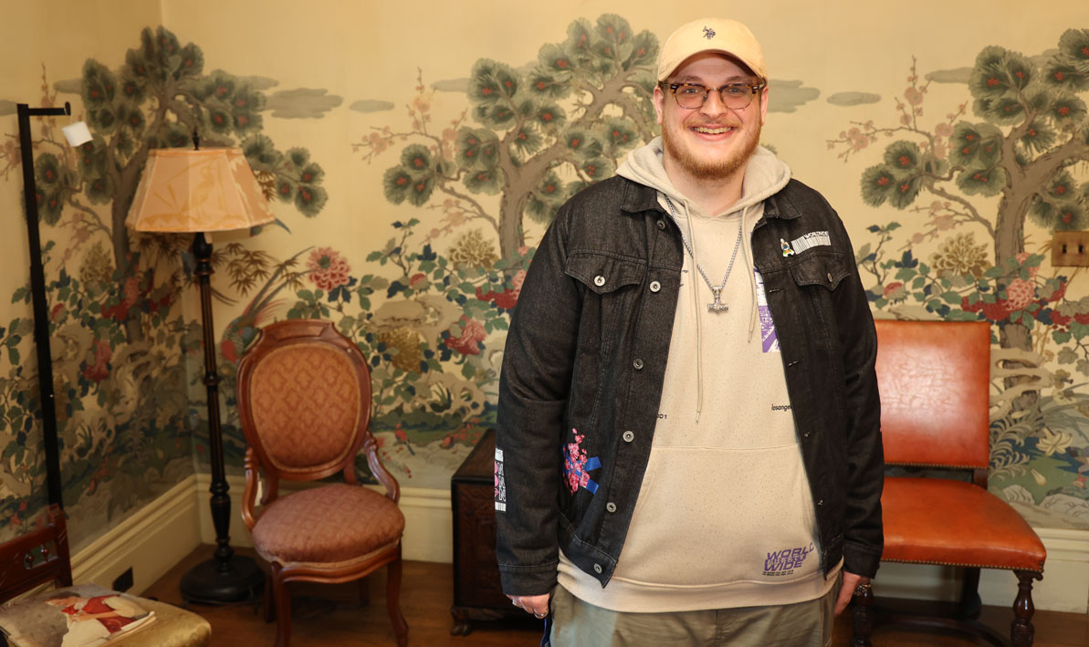 Animation student Alex Colson at Wistariahurst Museum stands next to the wallpaper that inspired him. 