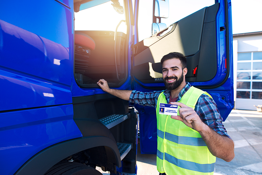 A CDL student holds up their license next to a blue truck