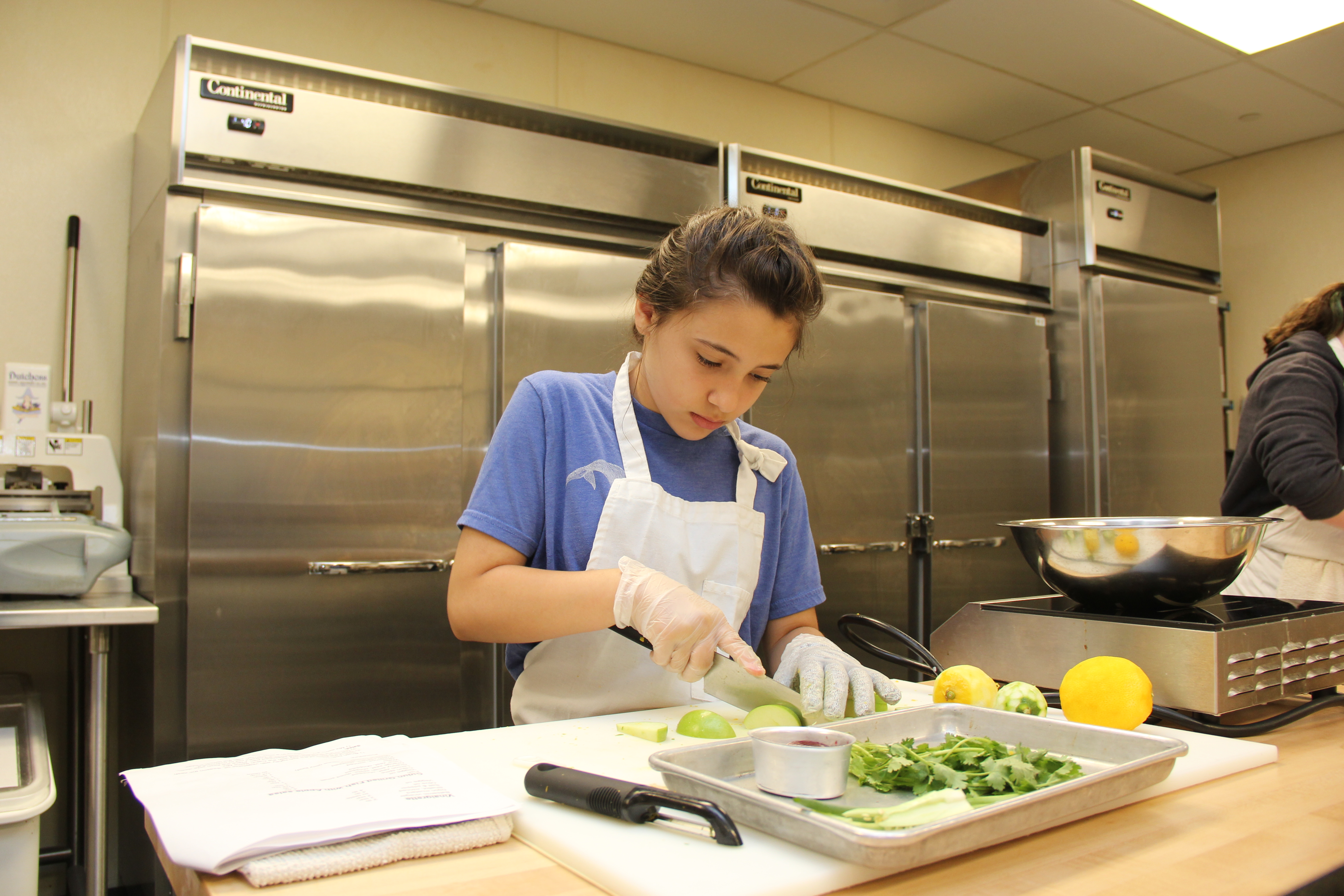 A student wearing an apron chops vegetables in a kitchen
